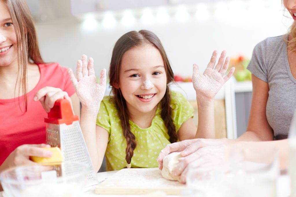 Portrait of happy girl showing her floured palms with her mother and sister near by